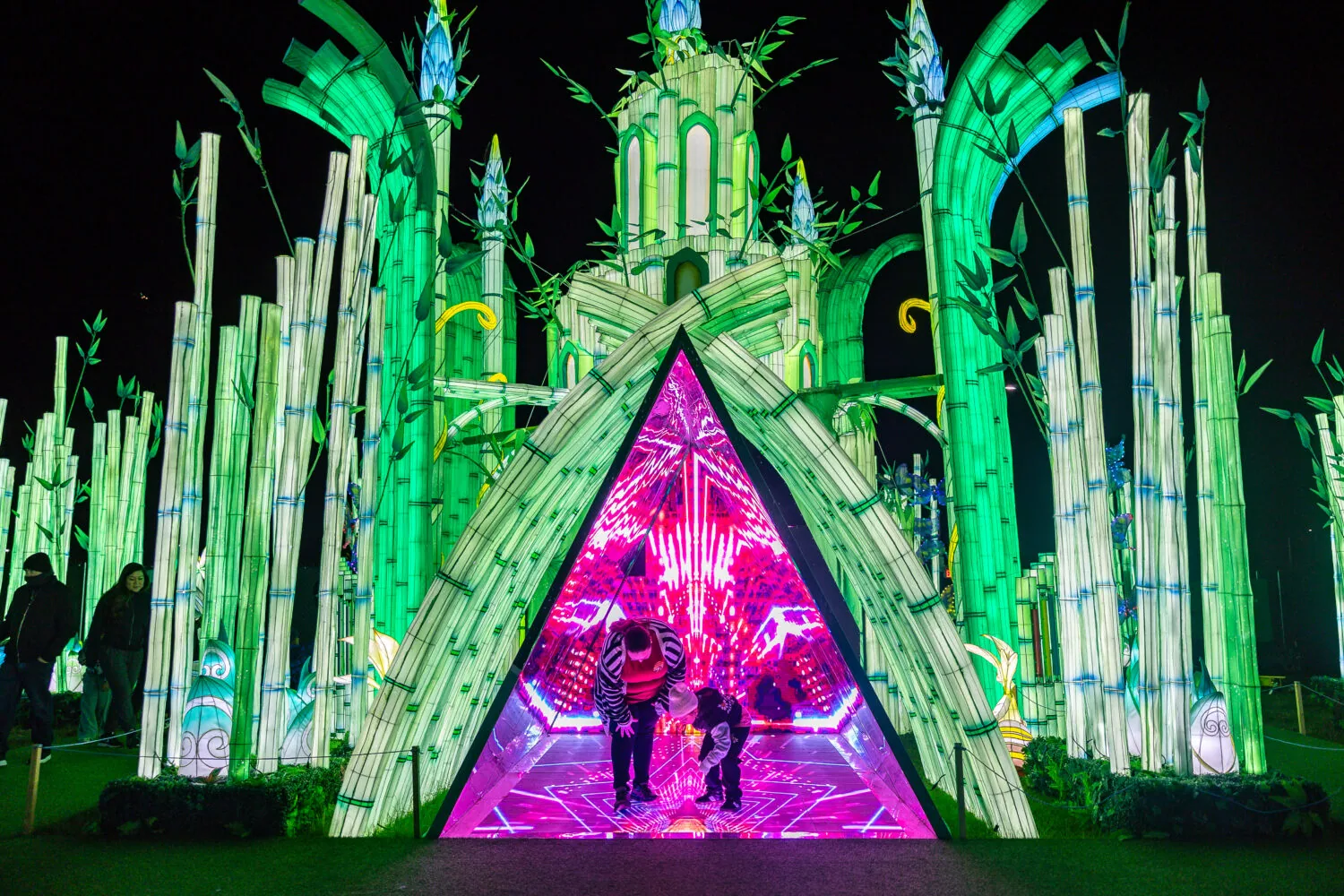 Visitors entering a glowing green lantern palace at Bright Nights at Four Mile in Denver